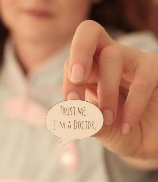 Женщина держит значок «Trust me, I'm a doctor»